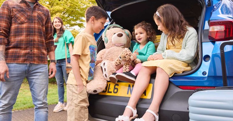 Children sit in the open boot of a car with teddy bear