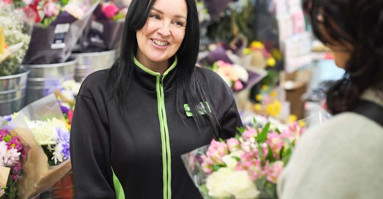 A shop worker talks to a customer who holds some flowers