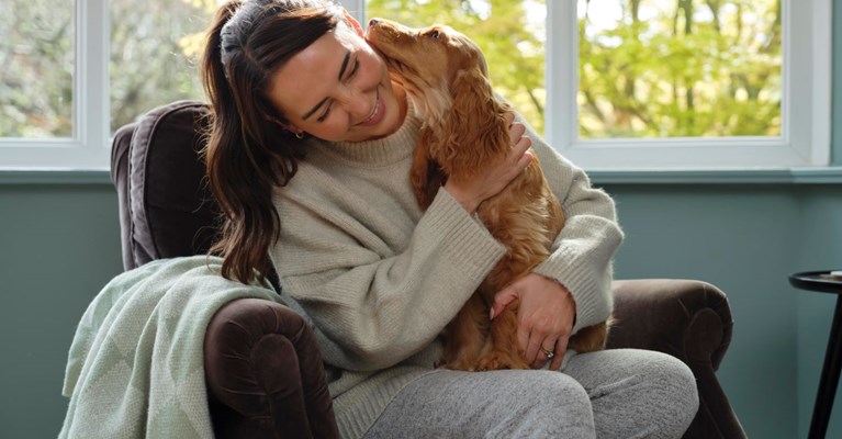 A woman hugs her dog on a sofa chair