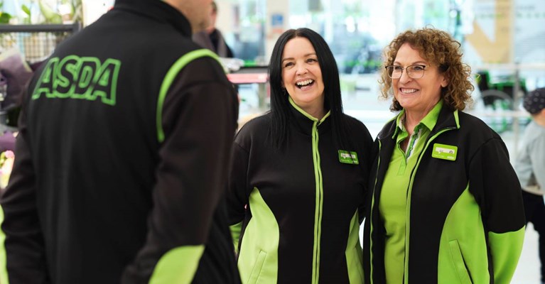 Asda workers stand talking and smiling on the shop floor