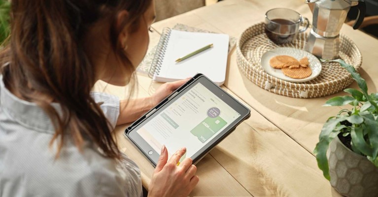 A woman sits at a table and looks at credit cards on the Asda Money website