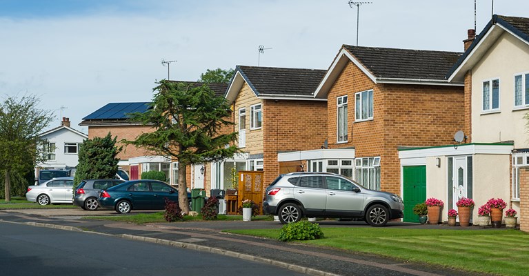 Four different coloured cars sat on the driveway of their separate detached houses 