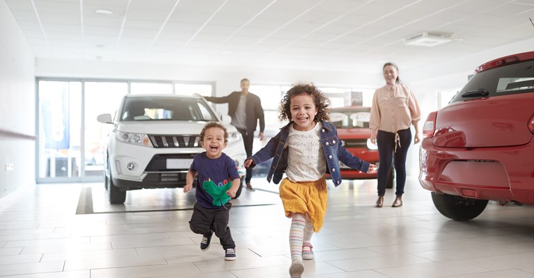 Two young children excitedly running through car showroom