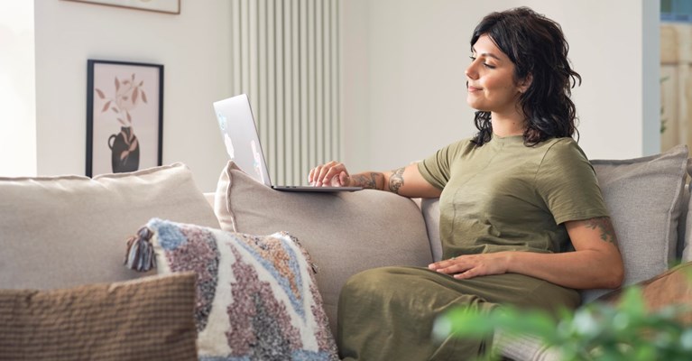 A woman sits on a sofa looking at a laptop