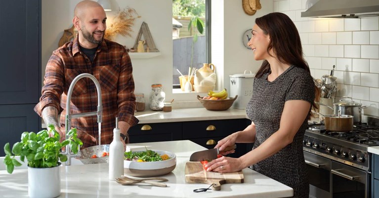 A man and a woman prepare a salad at a kitchen counter