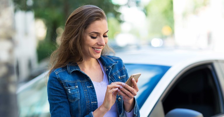 Woman stood in front of new car buying car insurance on mobile phone
