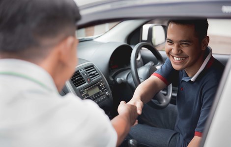 Smiling man sat in car shaking hands with salesman after buying new car