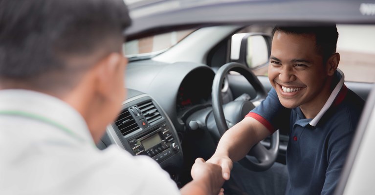 Smiling man sat in car shaking hands with salesman after buying new car