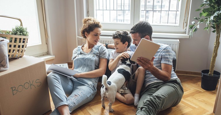 Young family and dog in home sat on wooden floor with mobile tablet