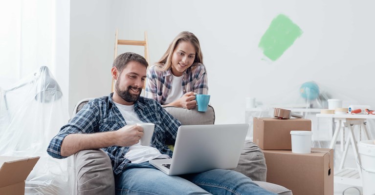 Young couple relaxing in new home reviewing financial services on laptop