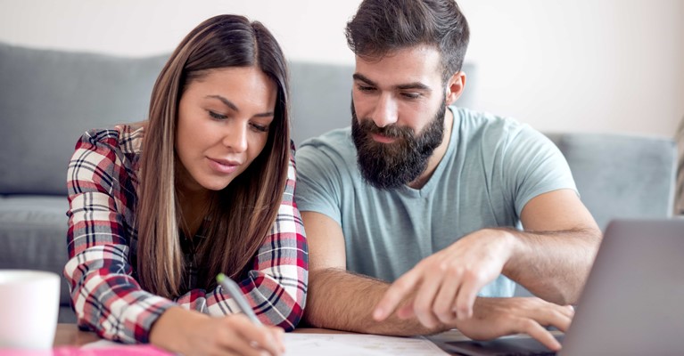 Young couple on laptop reviewing their finances using calculator pen and paper