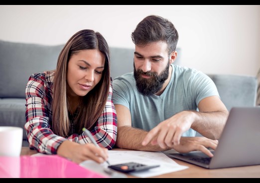 Young couple on laptop reviewing their finances using calculator pen and paper
