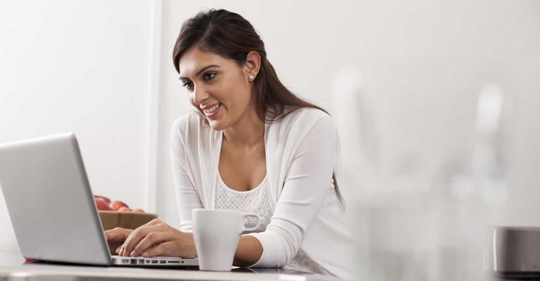 Smiling woman with drink reviewing financial services on laptop