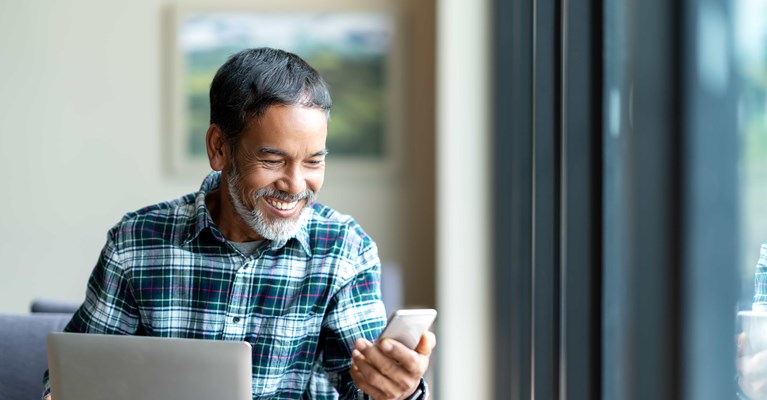 Older man using mobile phone and laptop to review financial services