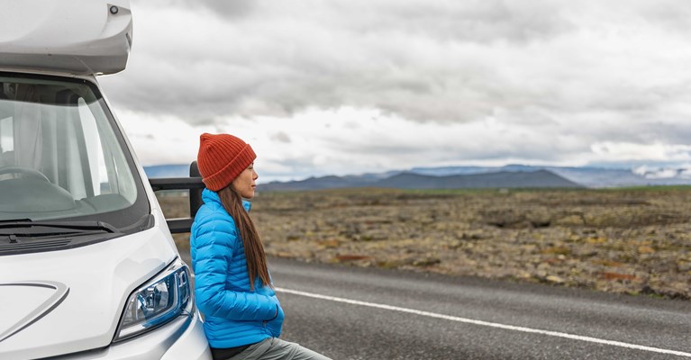 Woman in red hat and blue coat leaning on campervan