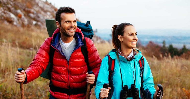 Backpacker couple on holiday wearing coats and hiking with binoculars and sticks