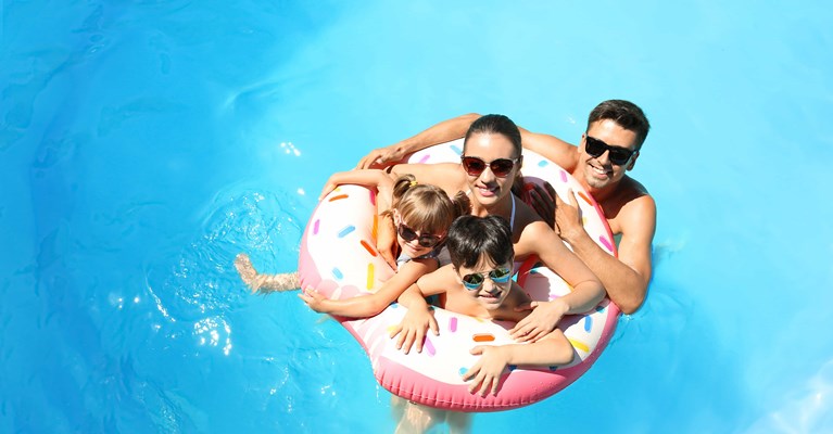 Happy family wearing sunglasses sharing an inflatable ring in a holiday swimming pool
