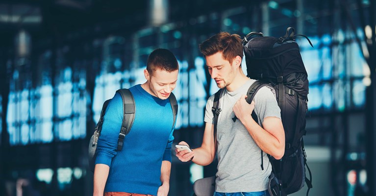 Two men wearing backpacks looking at booking reference on phone