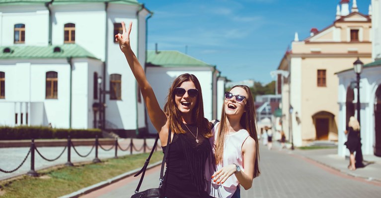 Two girls laughing and posing for selfie on holiday in front of idyllic buildings and river