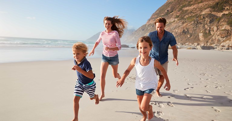 Smiling family on holiday running on a beach with mountains in background