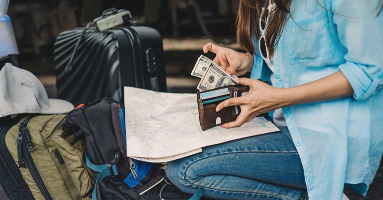 Woman with backpack and suitcase checking travel money banknotes in wallet