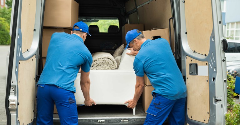 Two men in blue workman uniforms unloading furniture at a new home