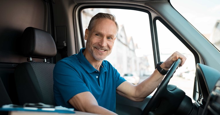 Smiling man with blue shirt driving a delivery van