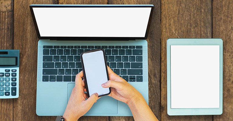 Hands using a phone, laptop, calculator and tablet