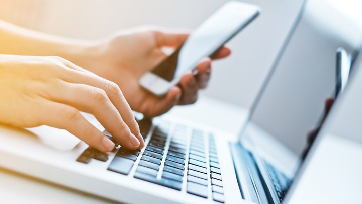 hands on a laptop, also using cell phone