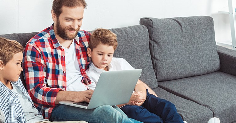 father and two sons sit on sofa using a laptop