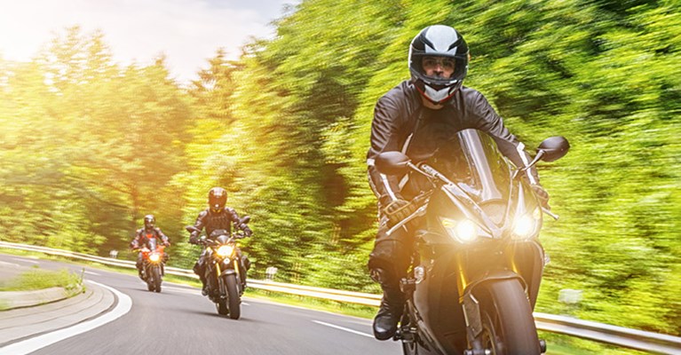 3 Motorcyclists driving down a leafy road