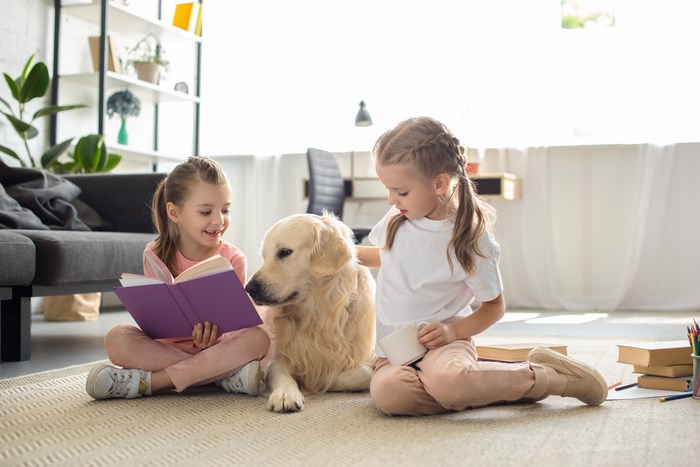 Little sisters with books and golden retriever dog near by sitting on floor at home