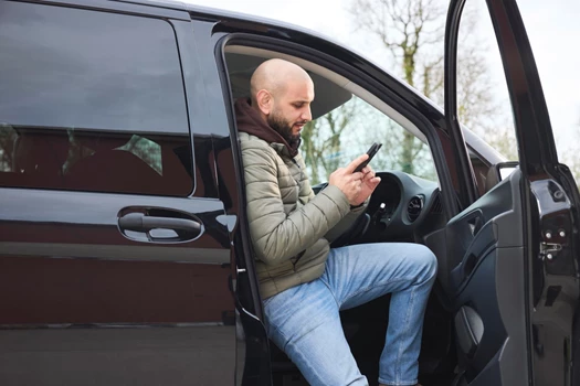 A man steps out of his car and looks at his phone