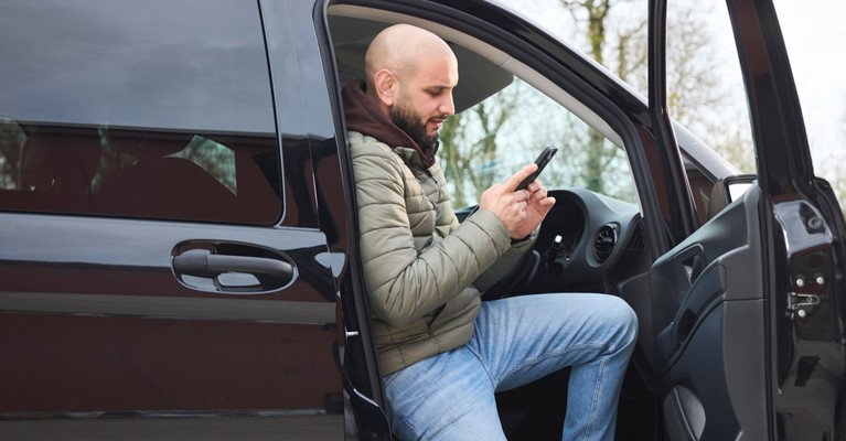 A man steps out of his car and looks at his phone
