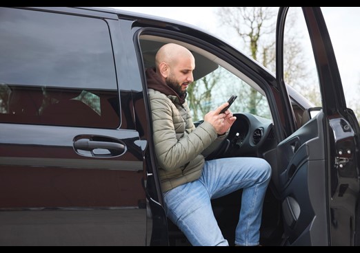 A man steps out of his car and looks at his phone