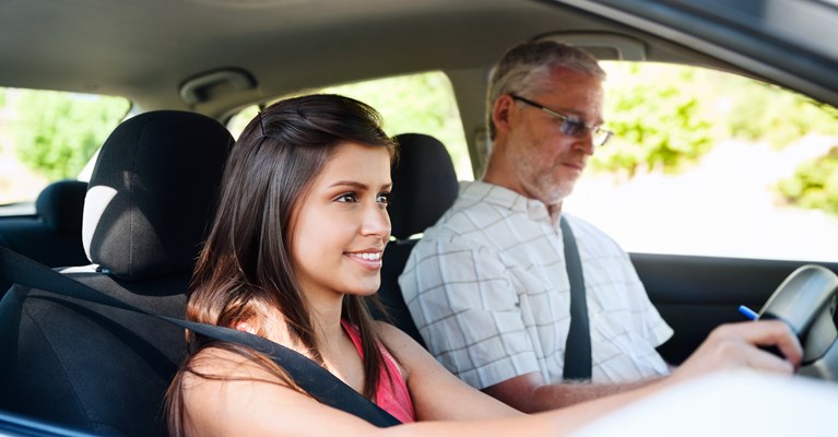 Young girl in the driving seat of a car on her driving lesson with instructor taking notes in the passenger seat