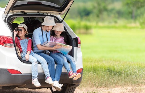 Mum and two children sat in the boot of their silver car looking at a map whilst the car is parked up by a field