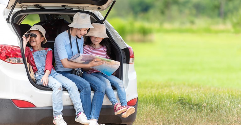 Mum and two children sat in the boot of their silver car looking at a map whilst the car is parked up by a field