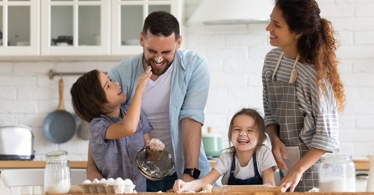 Young family of four having fun with the baking flour whilst baking cakes in their new kitchen on a summers day