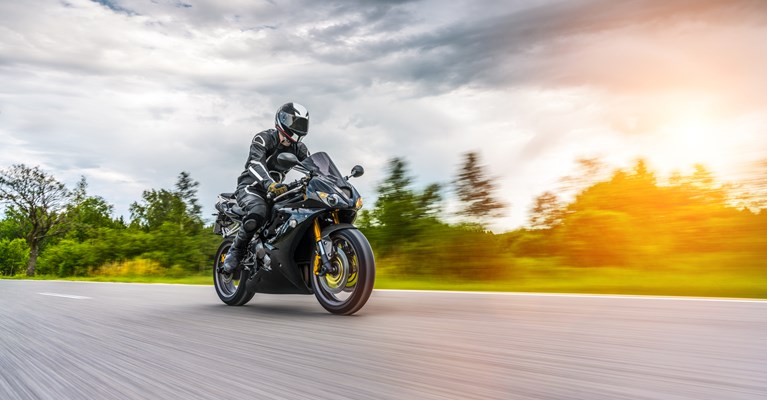 Person riding a new black motorbike wearing a black helmet and black safety jacket, black safety boots and black safety pants