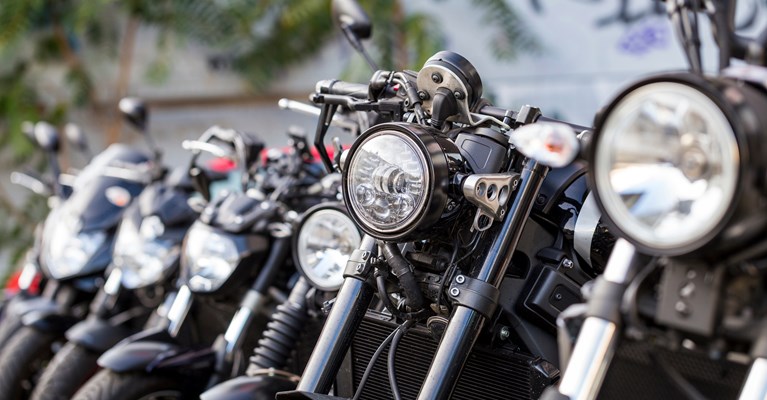 The headlights of several black motorbikes stood in a line parked up outside 