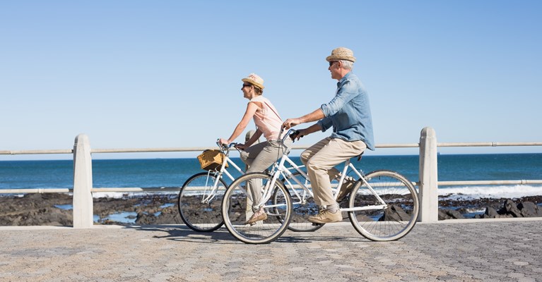 Couple wearing summer clothes and hats riding vintage bikes across the English coast