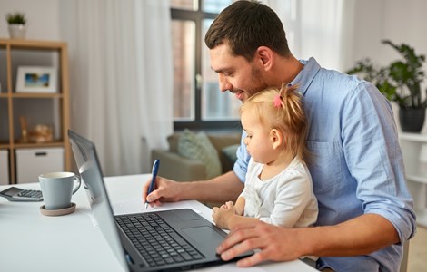 Dad sat with young daughter on his knee at the laptop writing notes