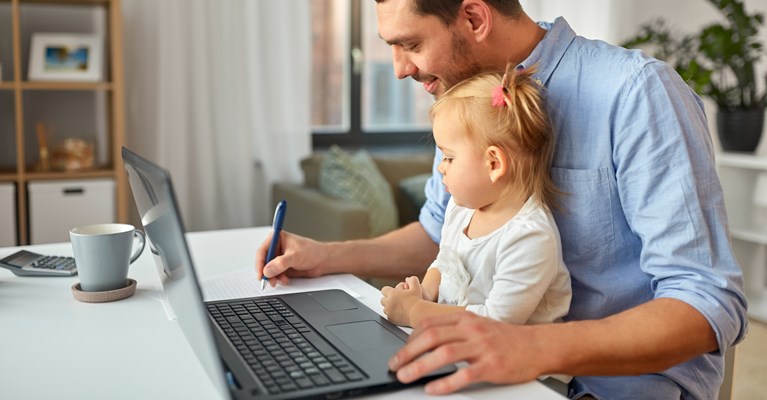 Dad sat with young daughter on his knee at the laptop writing notes