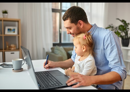 Dad sat with young daughter on his knee at the laptop writing notes
