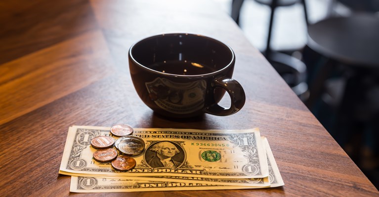 Dollars tip on a table beside a coffee