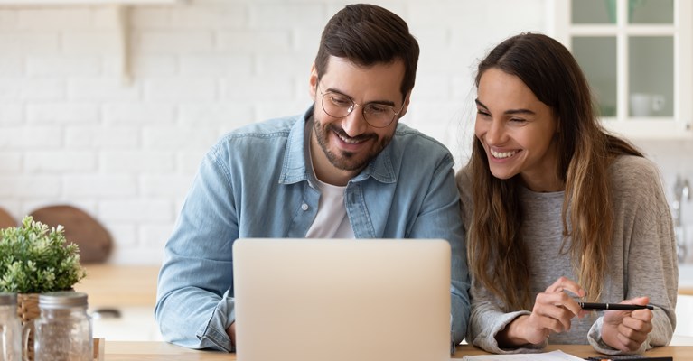 Couple sat in kitchen at laptop smiling and planning