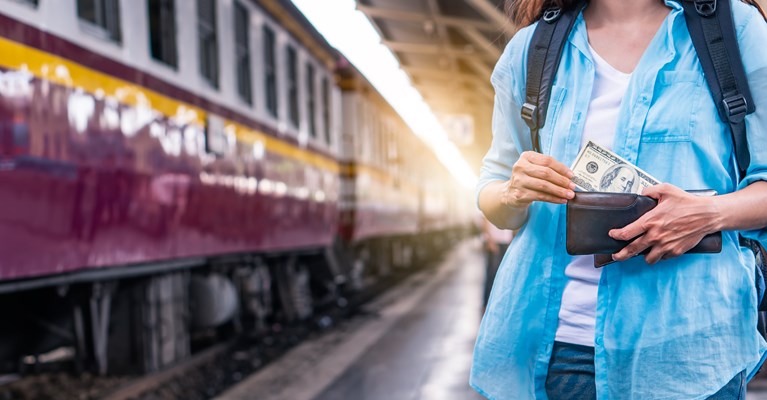 Female stood besides train with backpack and wallet with dollars