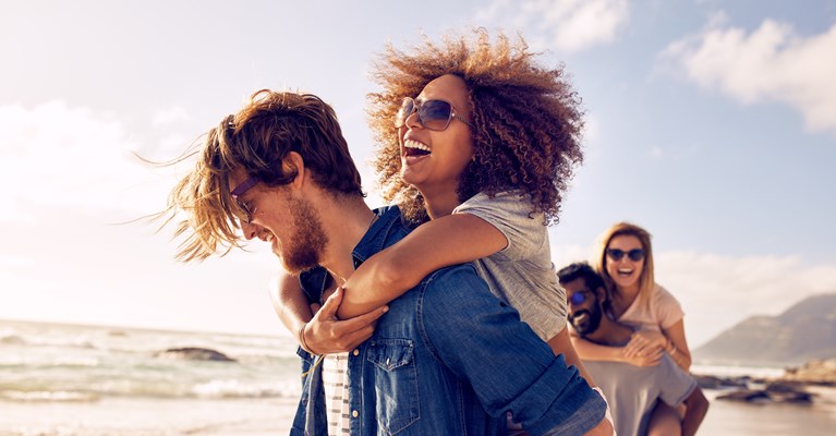 Two couples doing piggyback rides on beach