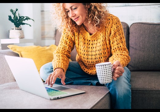 Woman sat on sofa wit a hot drink looking at laptop
